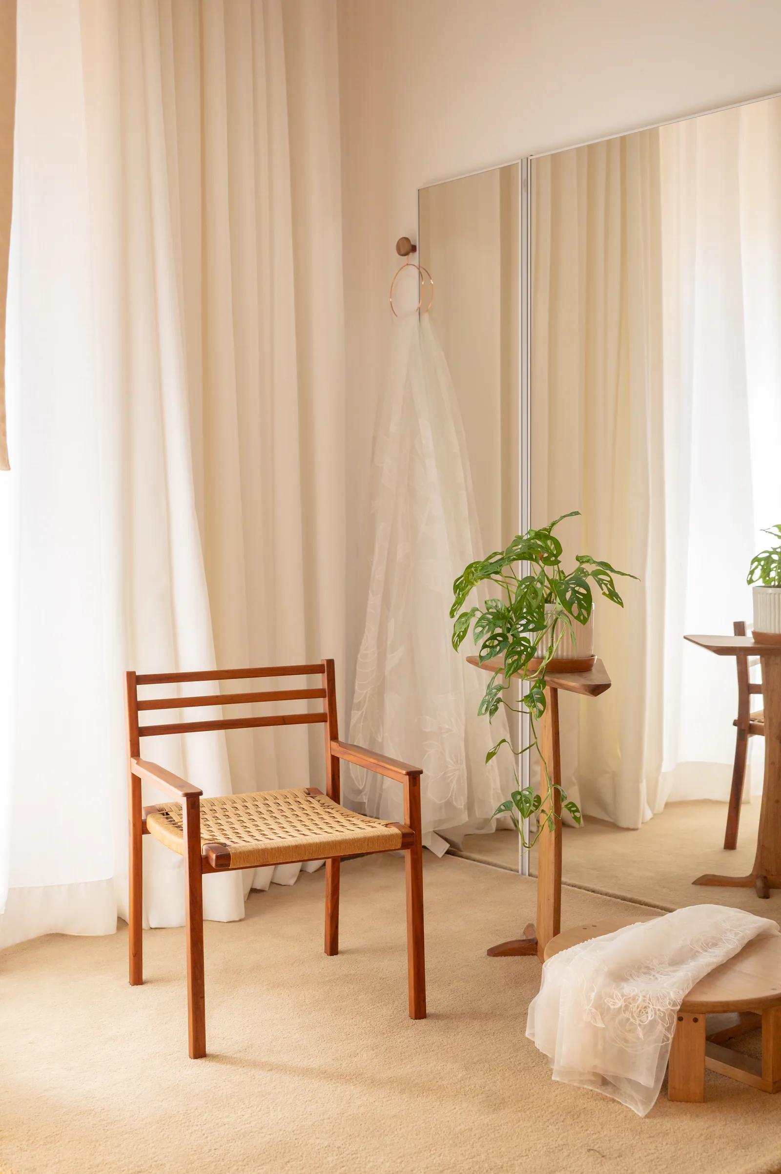 Provador da Casa Belina com cortinas claras, cadeira de madeira, espelho e um véu pendurado